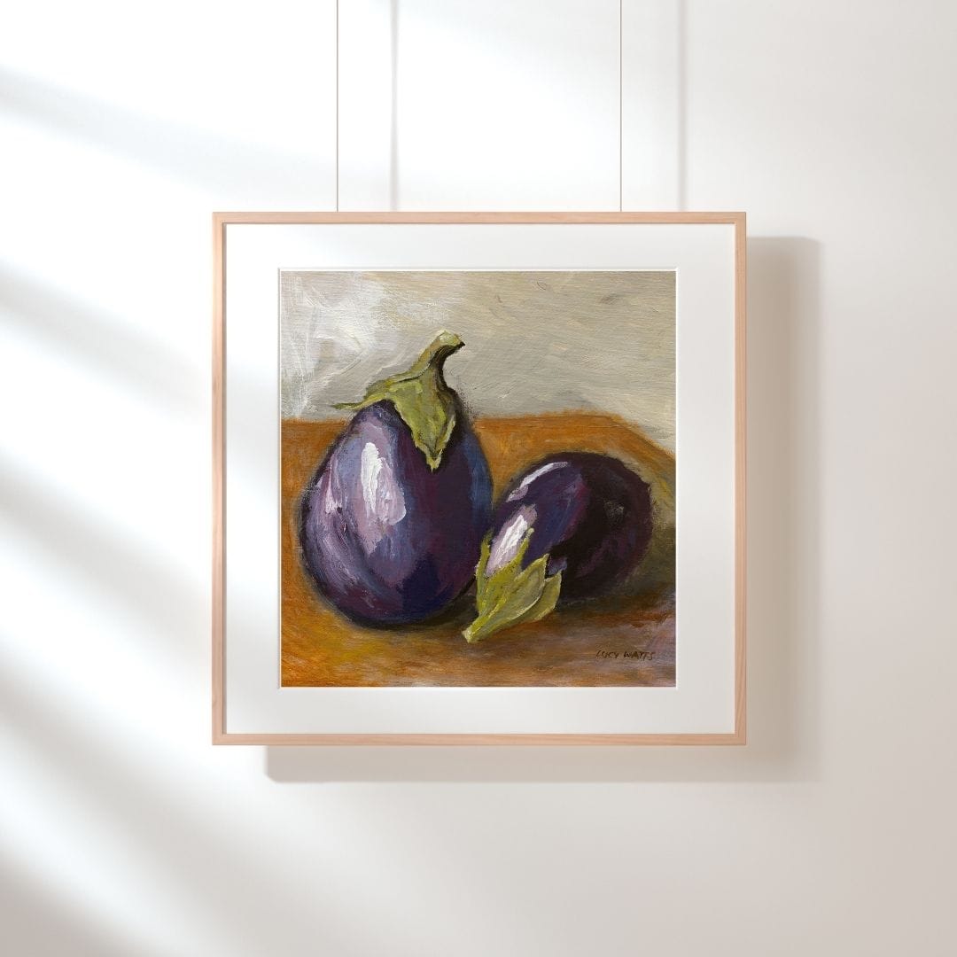 Framed painting of two eggplants on a wooden surface with a white background