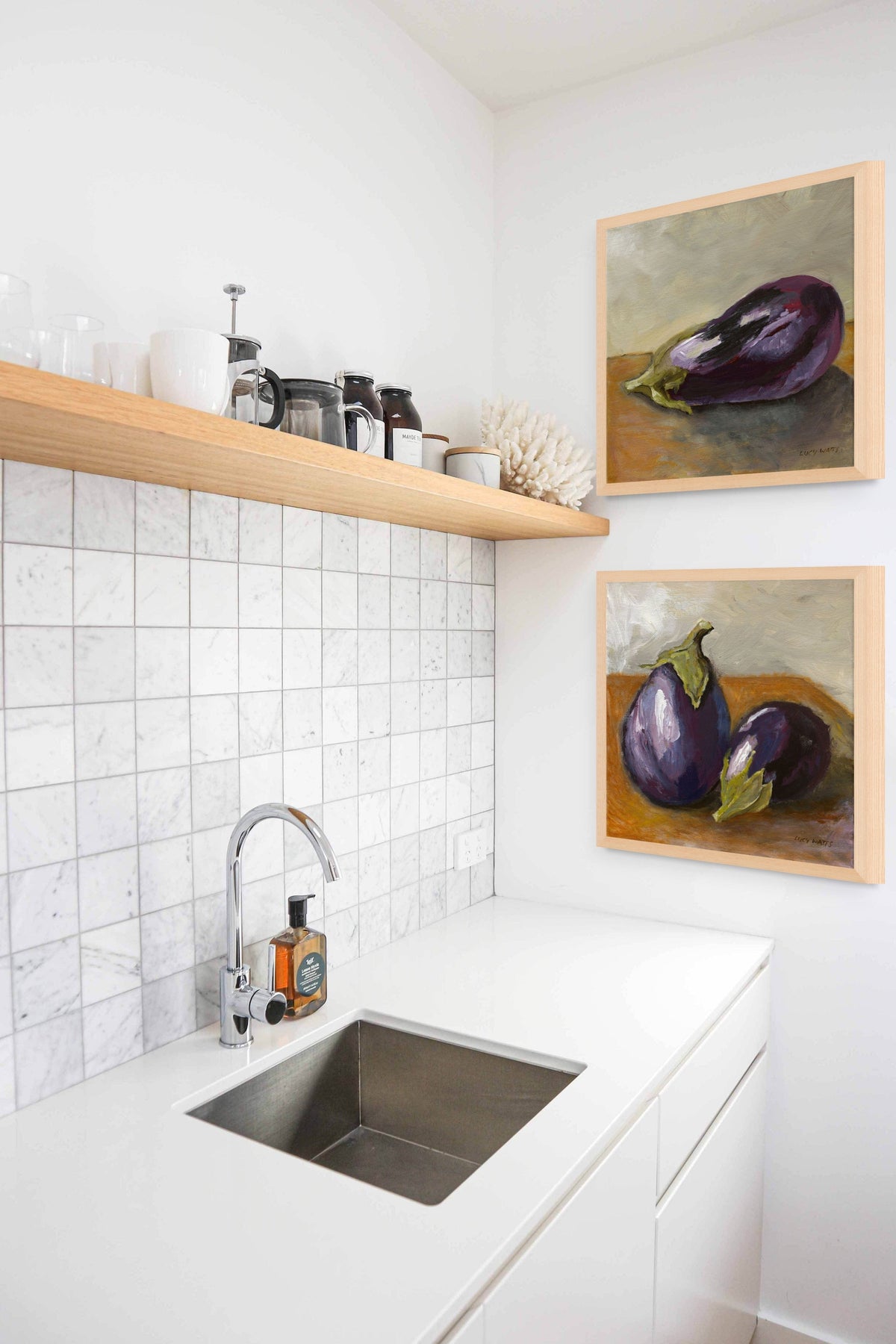 Kitchen with white tiled wall, wooden shelves, and framed artwork of eggplants.