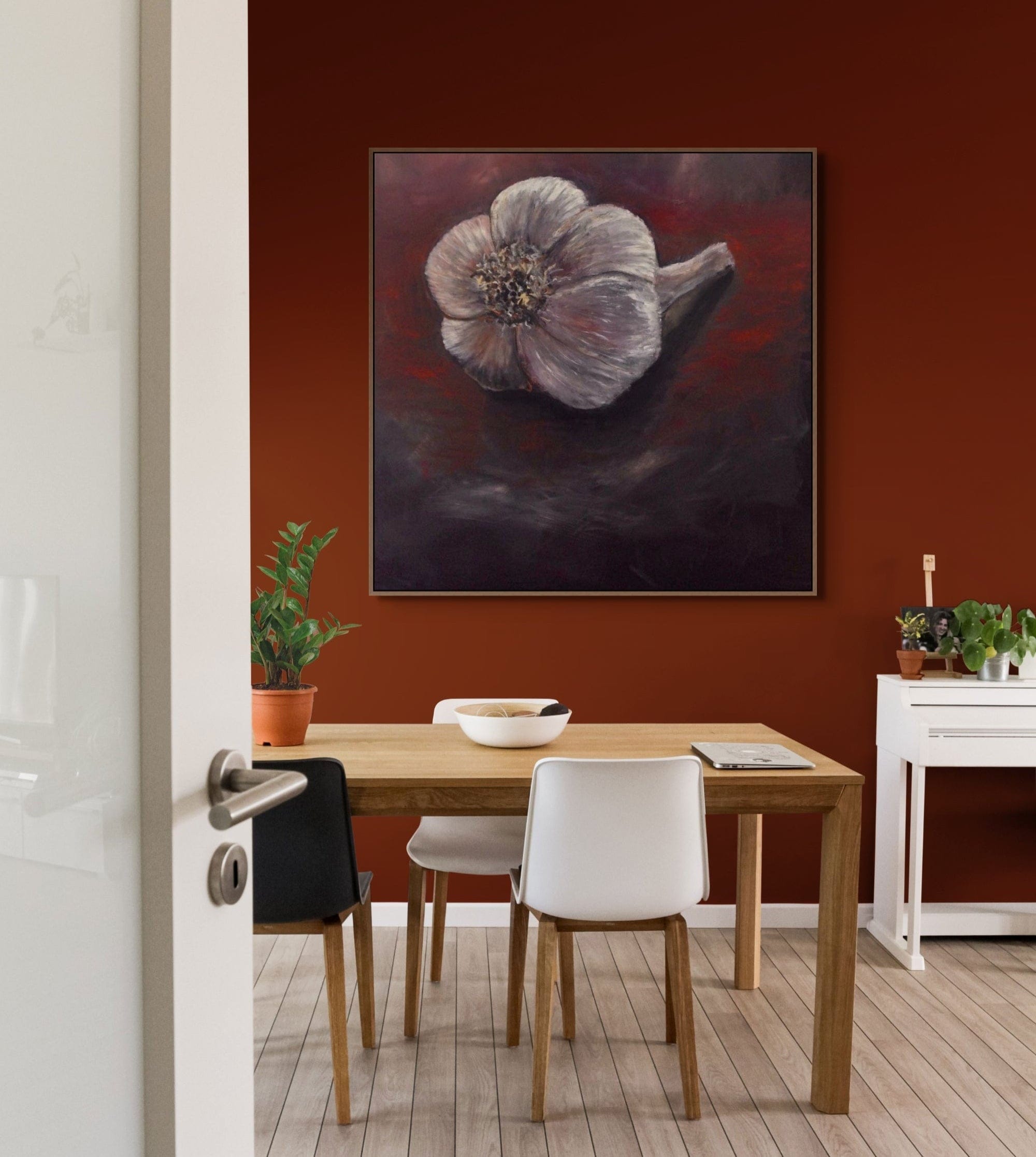 Dining room with a wooden table and chairs, a painting of a flower on the wall, and a plant on the table.
