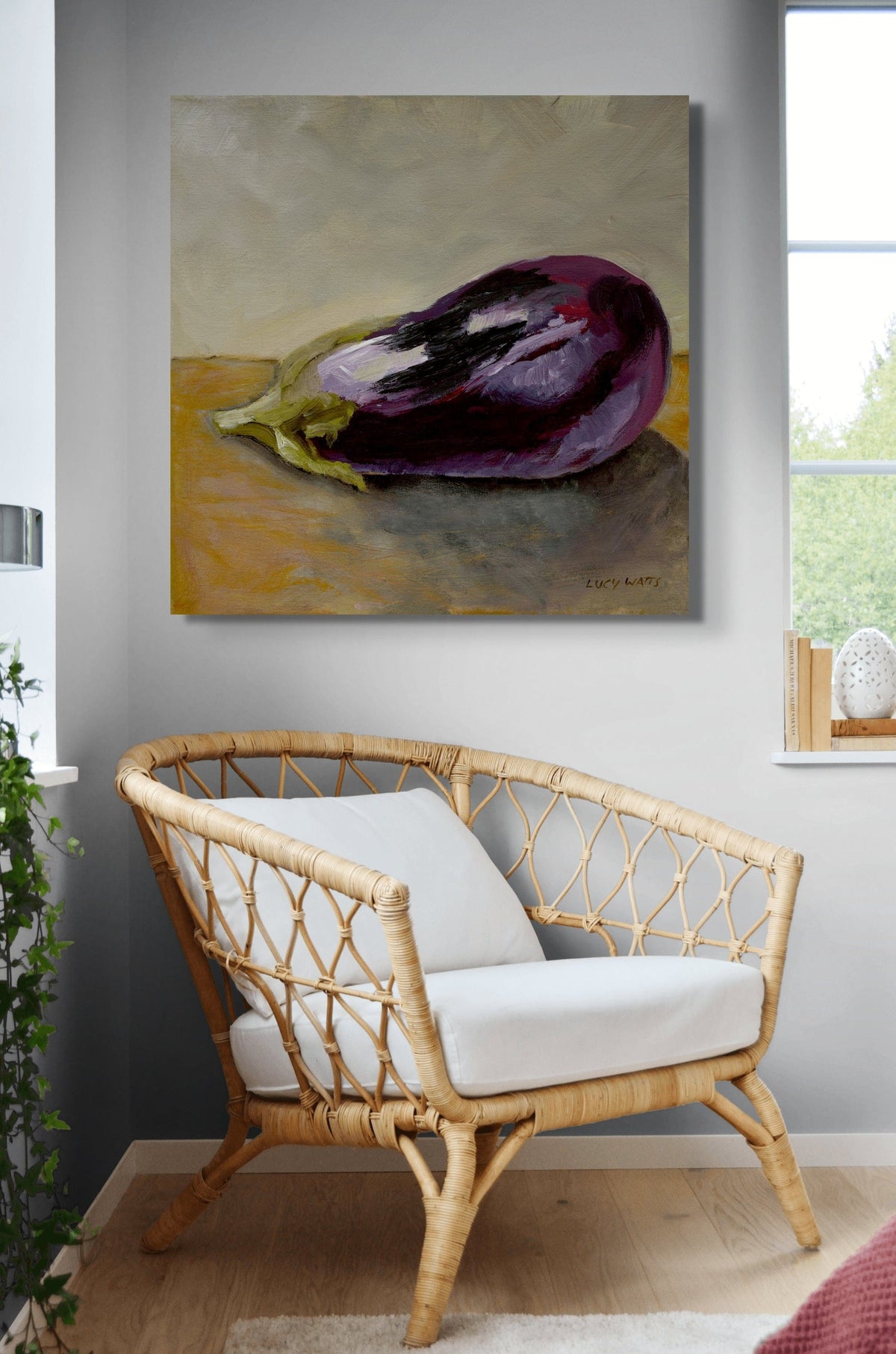 Rattan chair with white cushions in a room with a painting of an eggplant on the wall.