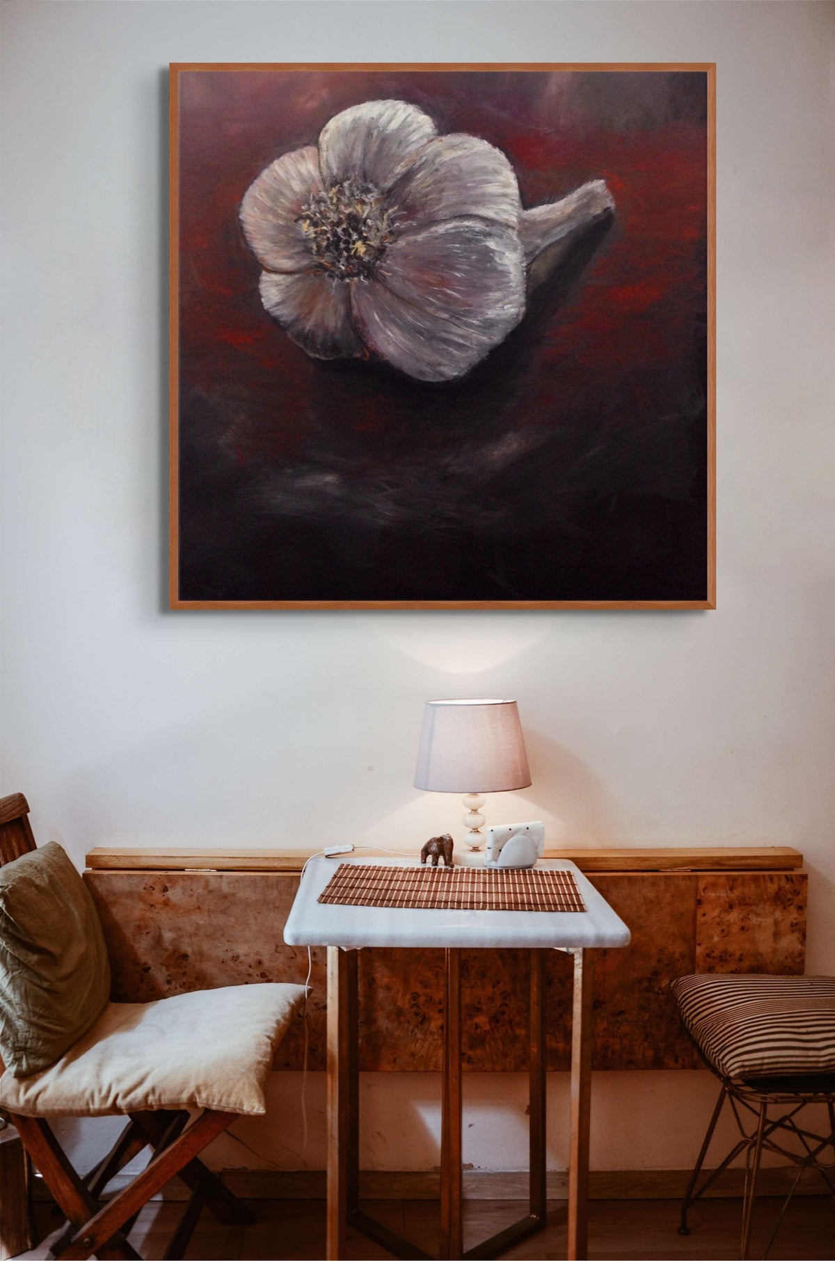 Framed painting of a flower on a wall above a table with a lamp and cushions.