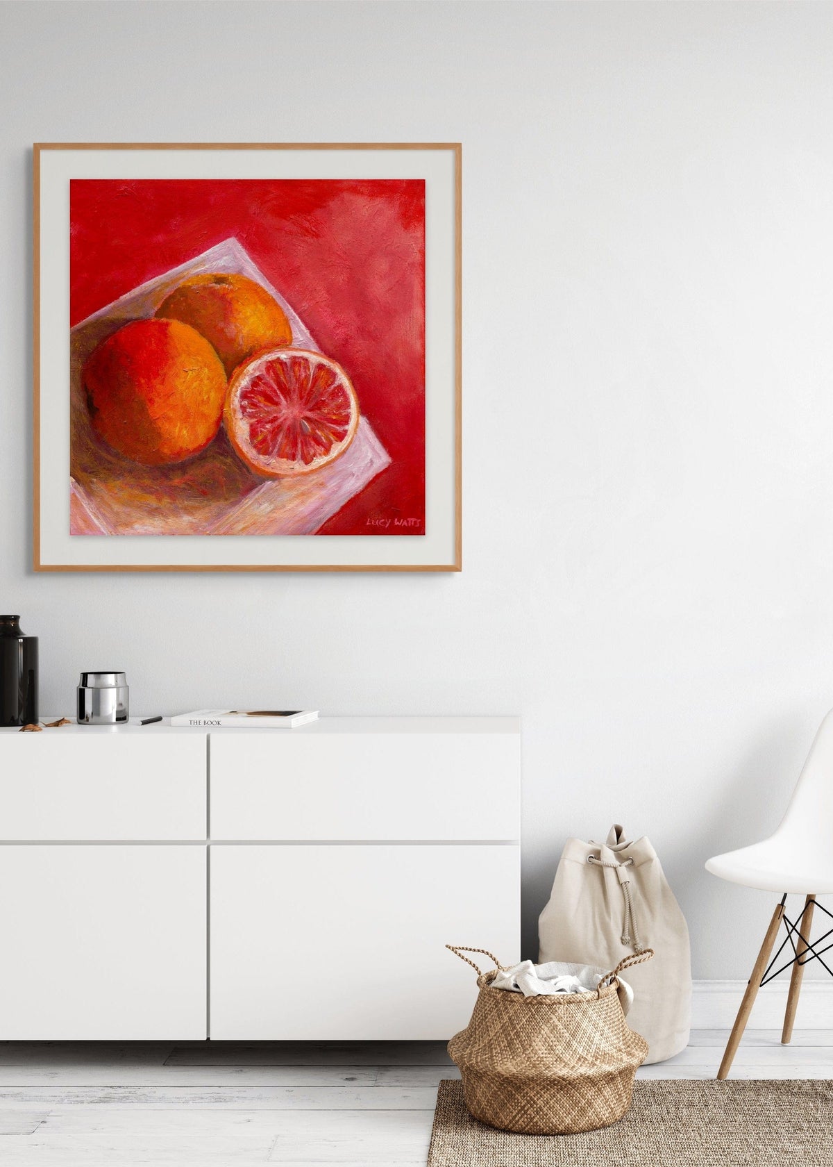 Framed print of original artwork by Australian artist Lucy Watts of grapefruits on white plate on a white wall above a white cabinet and homewares.