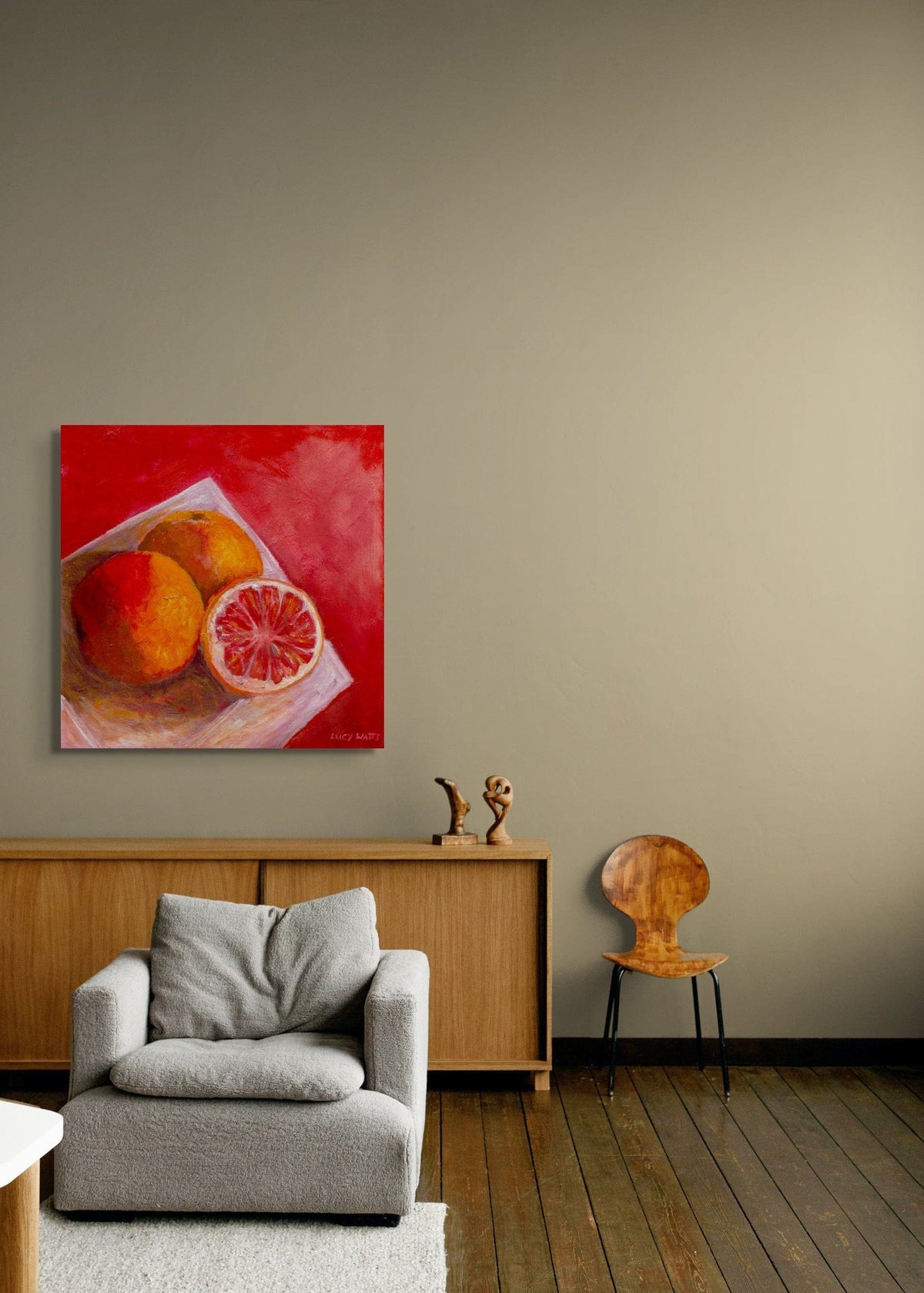Living room with a  print of original painting by Australian artist, Lucy Watts of  ruby grapefruits on the wall, gray sofa, wooden cabinet, and chair.