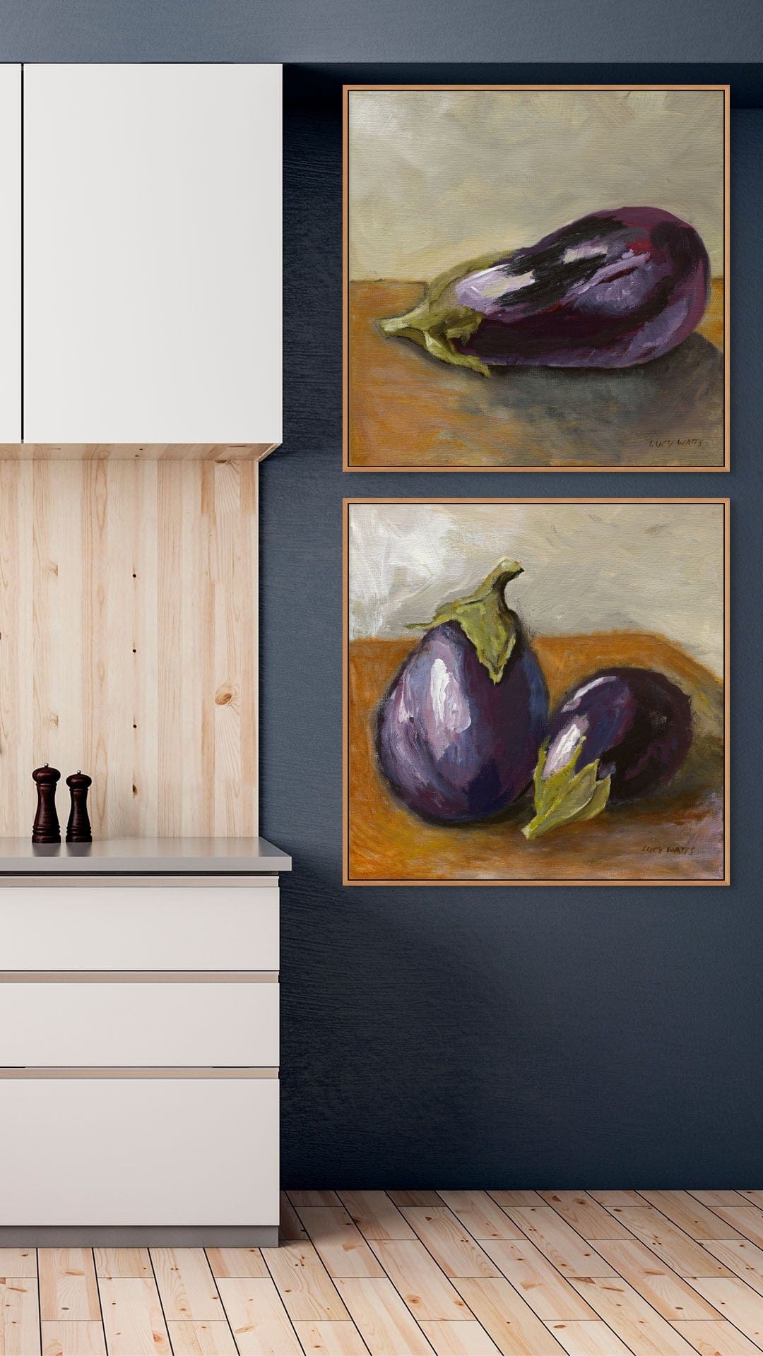Two paintings of eggplants on a wall above kitchen cabinets.