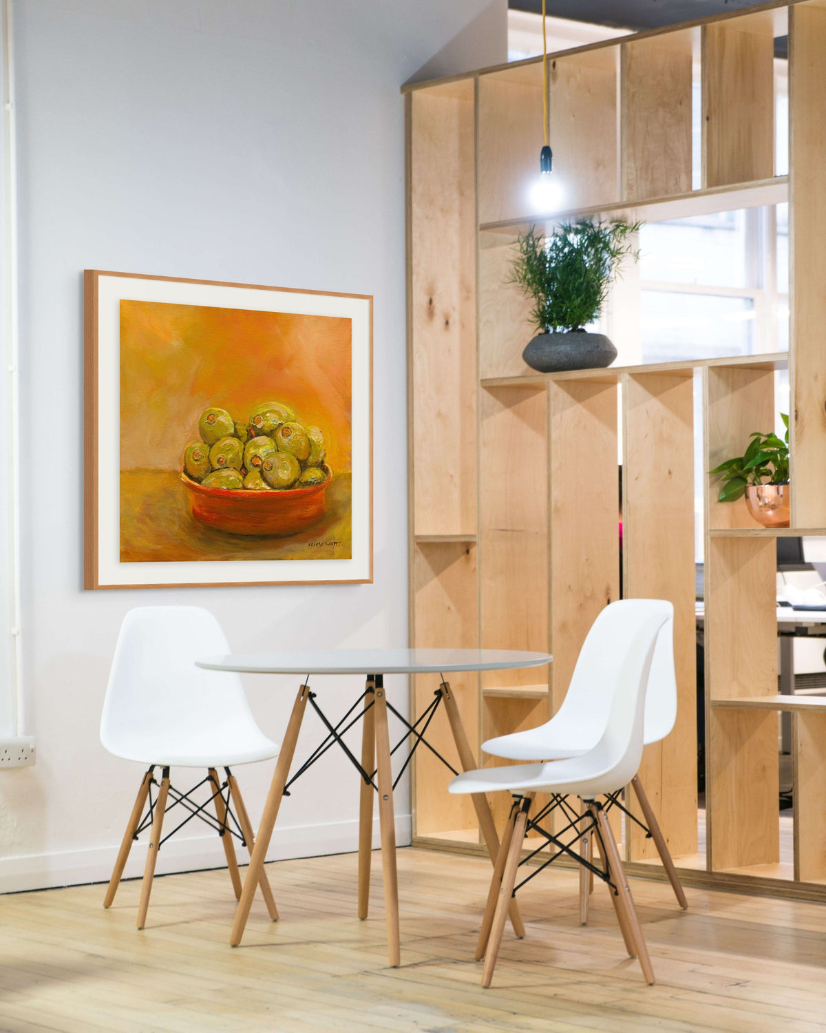 Modern dining area with white chairs, a round table, and a painting of apples on the wall.