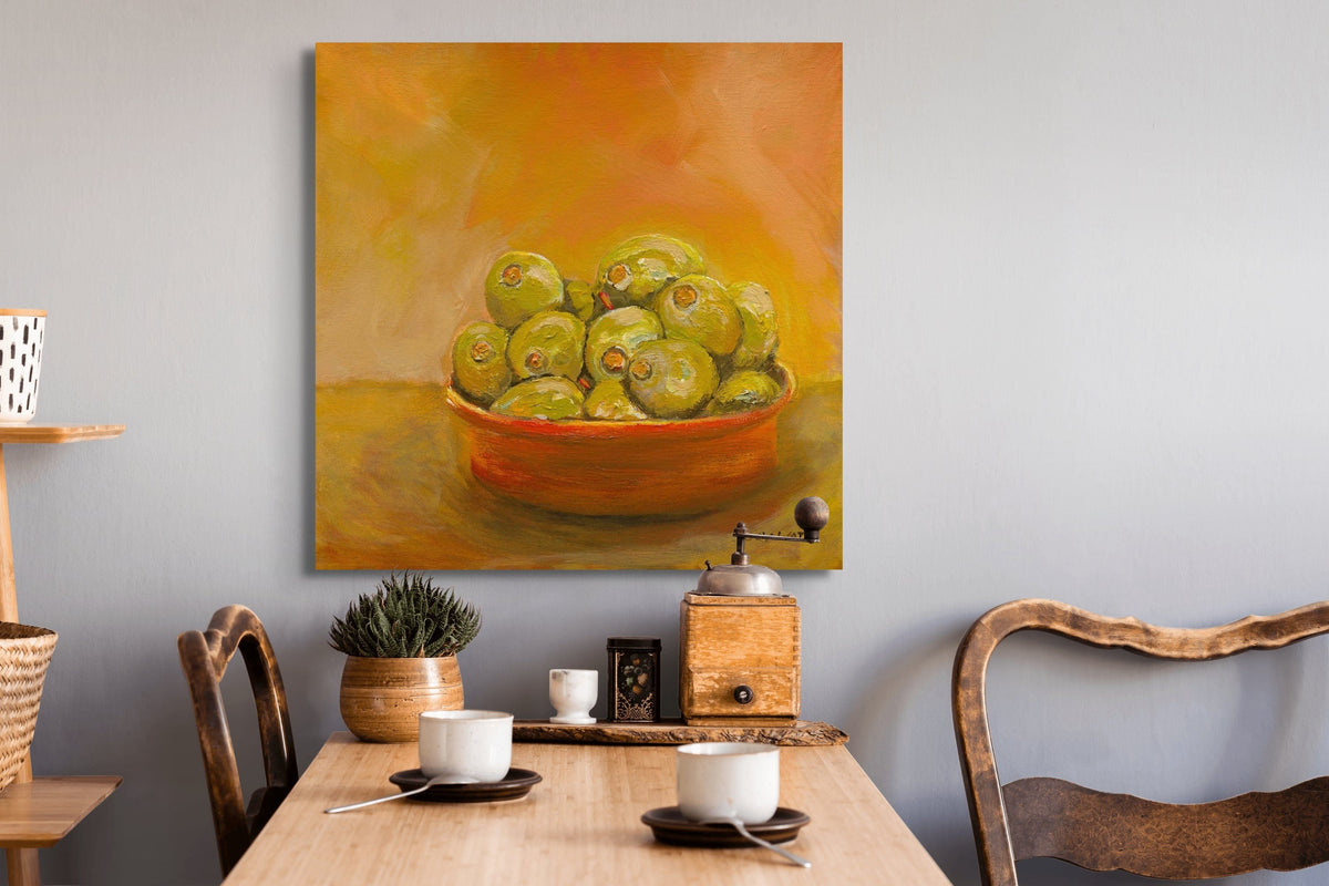 Painting of a bowl of green apples on a wall above a dining table with chairs.