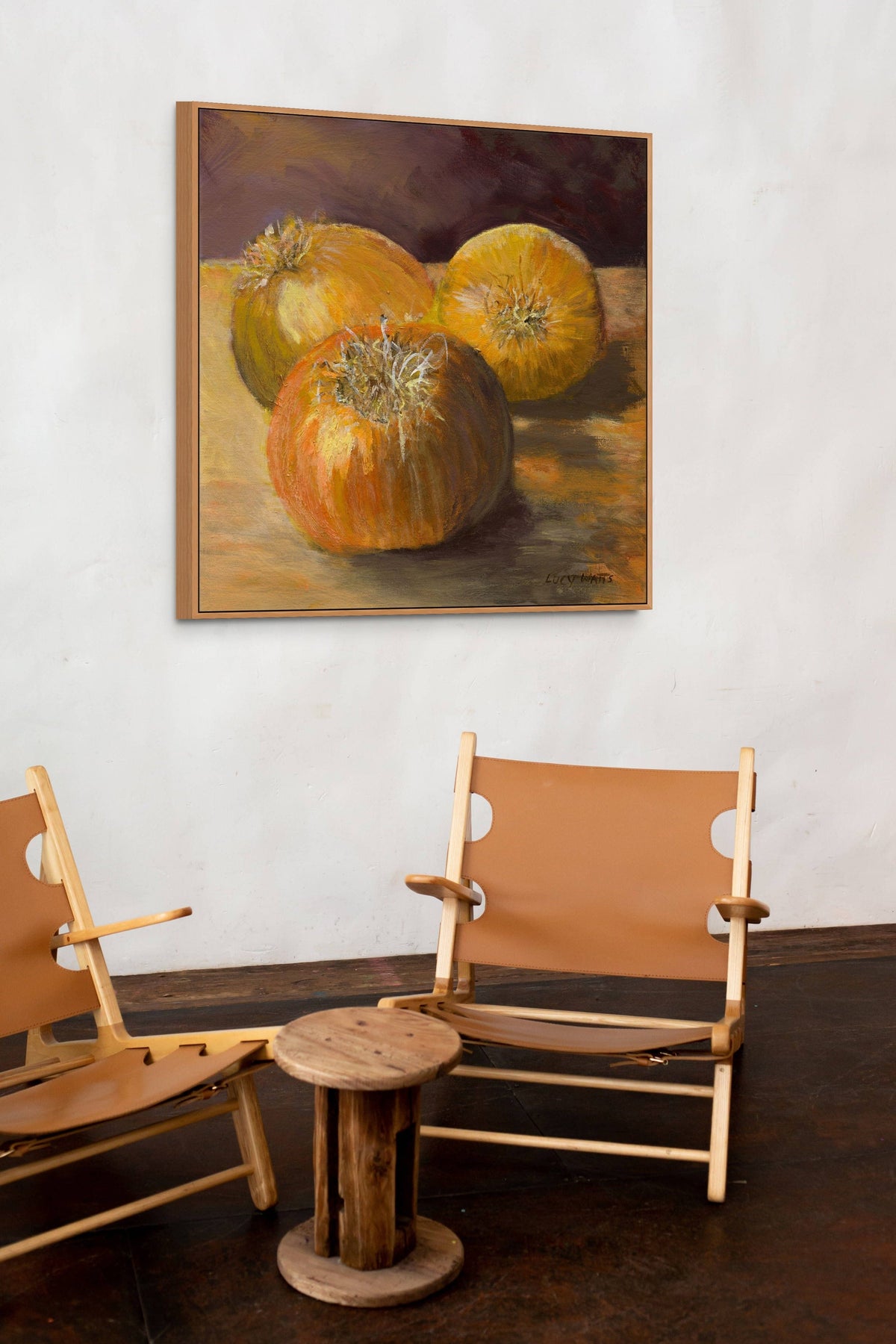 Two wooden chairs with a round wooden table in front of a painting of pumpkins on a white wall.