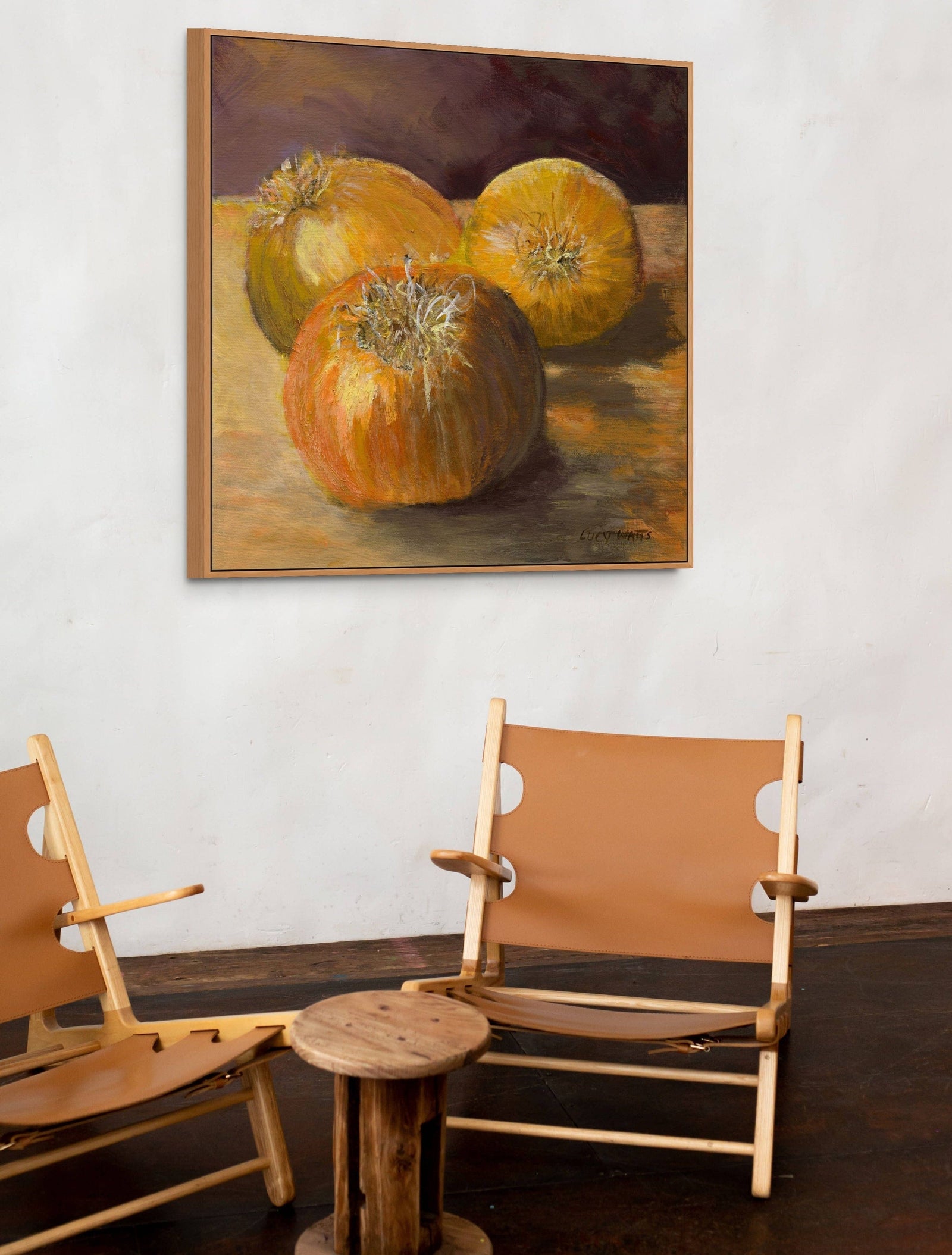 Two wooden chairs with leather seats and backs in front of a painting of pumpkins on a wall.
