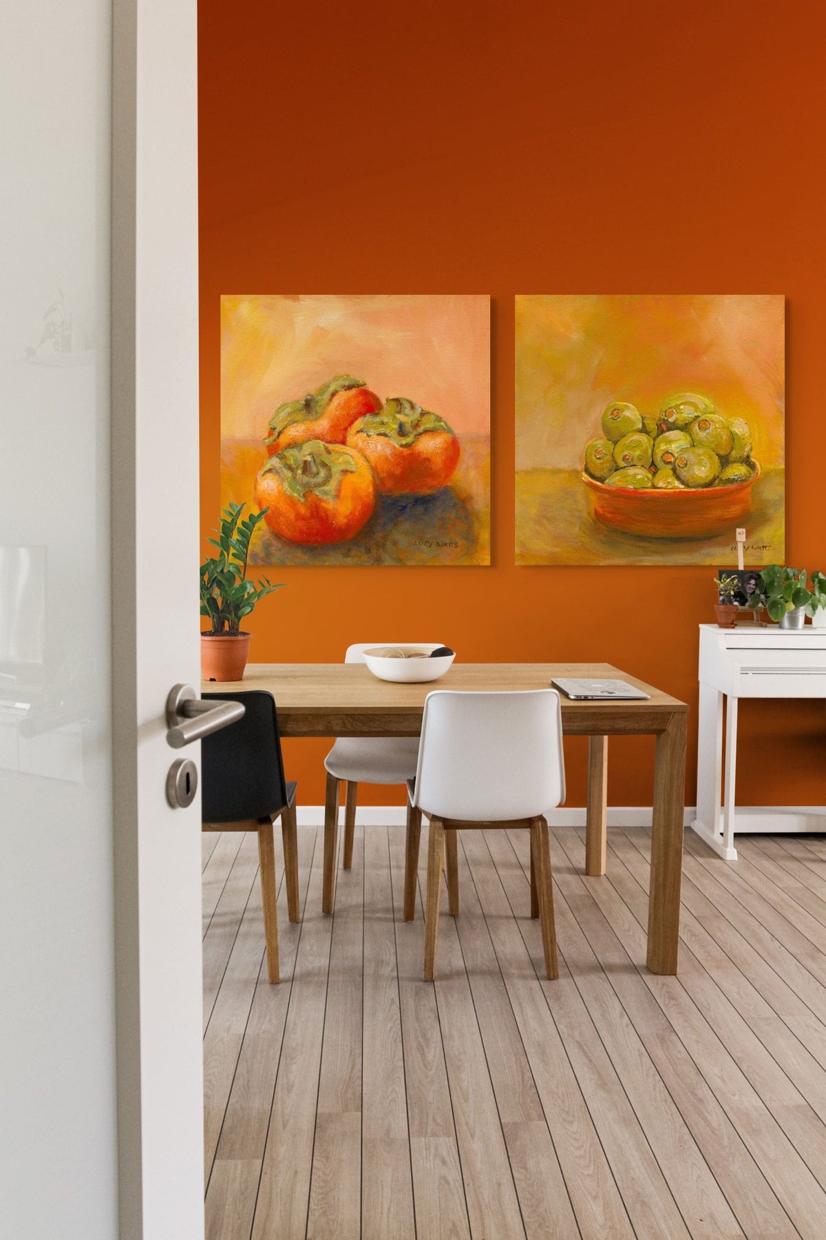Dining area with a wooden table and chairs against an orange wall with fruit paintings.
